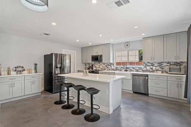 361 Whispering Hollow Dr, Kyle, TX 78640 - kitchen with appliances with stainless steel finishes, concrete flooring, tasteful backsplash, a kitchen bar, and a center island