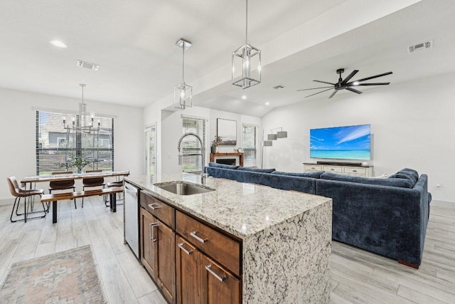 kitchen with a sink, light wood finished floors, light stone counters, pendant lighting, and recessed lighting