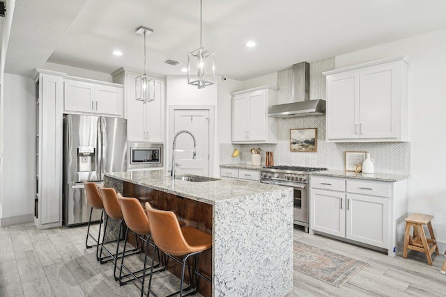 kitchen featuring wall chimney exhaust hood, appliances with stainless steel finishes, a sink, white cabinetry, and a breakfast bar