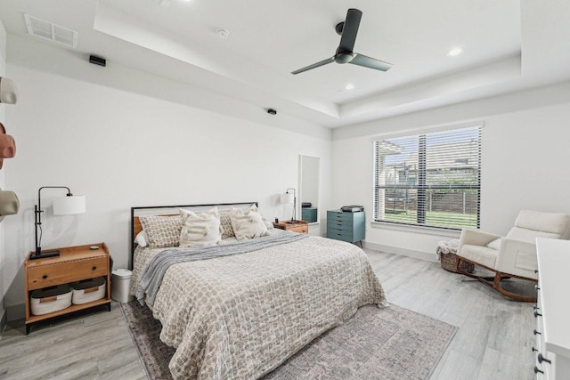 bedroom with a tray ceiling, light wood-style floors, recessed lighting, ceiling fan, and baseboards