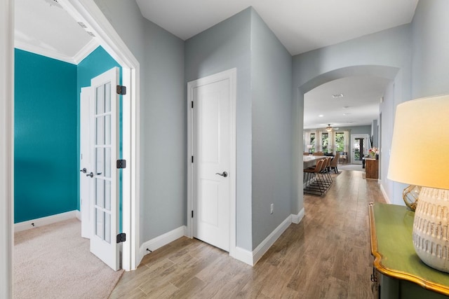 corridor with arched walkways, wood finished floors, baseboards, and french doors