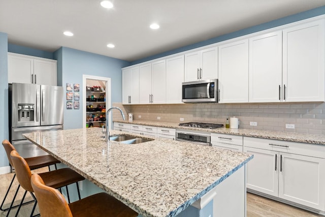 kitchen with stainless steel appliances, a sink, tasteful backsplash, a breakfast bar, and a kitchen island with sink