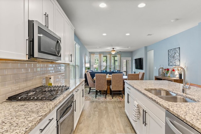 kitchen with appliances with stainless steel finishes, a sink, light wood finished floors, recessed lighting, and white cabinetry