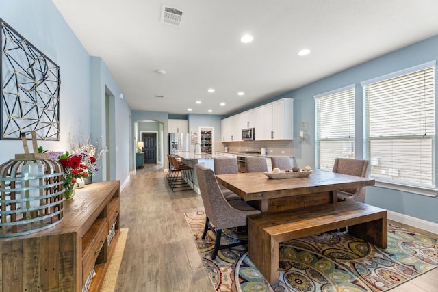 dining space featuring arched walkways, light wood-style floors, baseboards, and recessed lighting