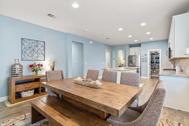 dining room featuring recessed lighting, light wood-style flooring, baseboards, and arched walkways