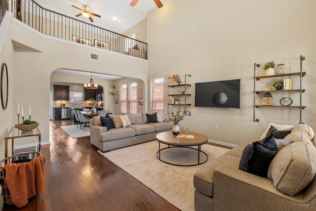 living room with arched walkways, ceiling fan, wood finished floors, baseboards, and a high ceiling