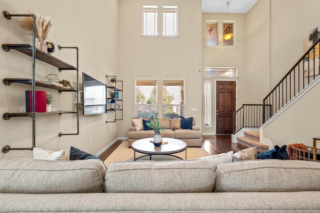 living area featuring wood finished floors, a towering ceiling, stairs, and baseboards