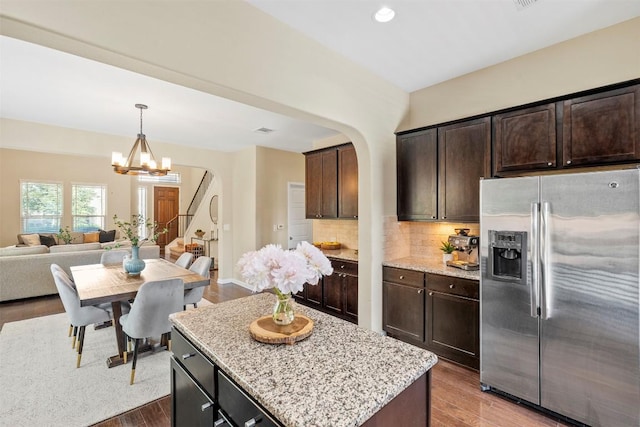 kitchen with stainless steel refrigerator with ice dispenser, arched walkways, open floor plan, a kitchen island, and wood finished floors