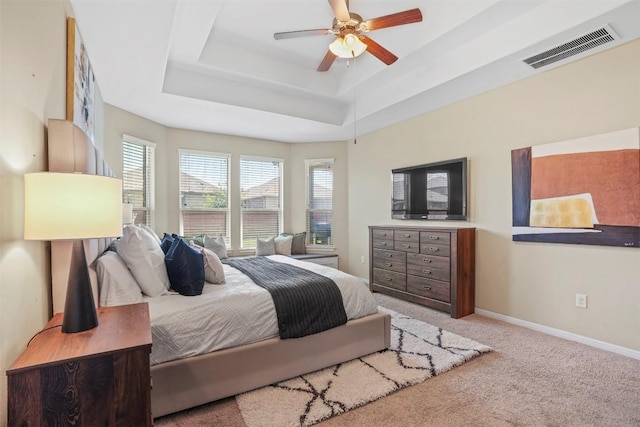 carpeted bedroom featuring multiple windows, a raised ceiling, baseboards, and a ceiling fan
