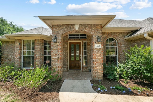 doorway to property with brick siding and roof with shingles