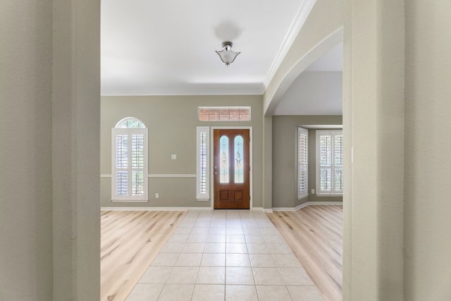 foyer entrance featuring plenty of natural light, ornamental molding, arched walkways, light tile patterned floors, and baseboards