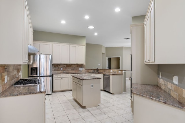 kitchen featuring appliances with stainless steel finishes, a sink, tasteful backsplash, a kitchen island, and dark stone counters