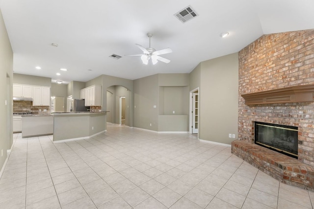 unfurnished living room with a ceiling fan, a brick fireplace, arched walkways, light tile patterned flooring, and baseboards