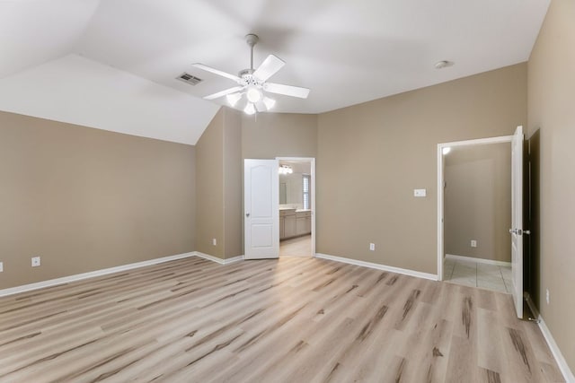 unfurnished bedroom featuring lofted ceiling, light wood-style floors, ensuite bath, a ceiling fan, and baseboards