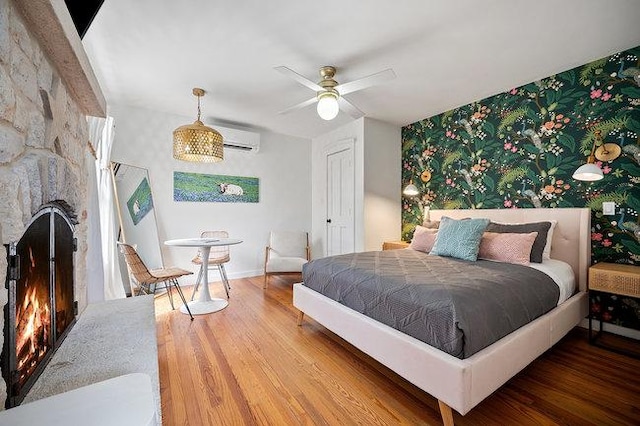 234 Loring, Stonewall, TX 78671 - bedroom with wallpapered walls, an accent wall, wood finished floors, a stone fireplace, and baseboards