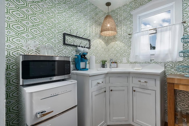 234 Loring, Stonewall, TX 78671 - kitchen featuring stainless steel microwave, wallpapered walls, light countertops, white cabinetry, and decorative light fixtures