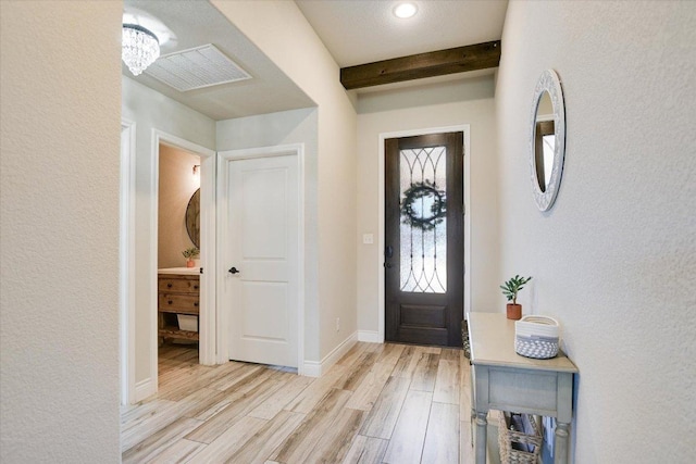 entrance foyer with light wood finished floors, beam ceiling, baseboards, and a textured wall