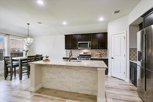 kitchen featuring stainless steel appliances, a sink, decorative backsplash, a chandelier, and light stone countertops