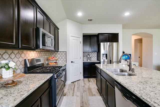 kitchen featuring appliances with stainless steel finishes, a sink, arched walkways, light wood finished floors, and light stone counters