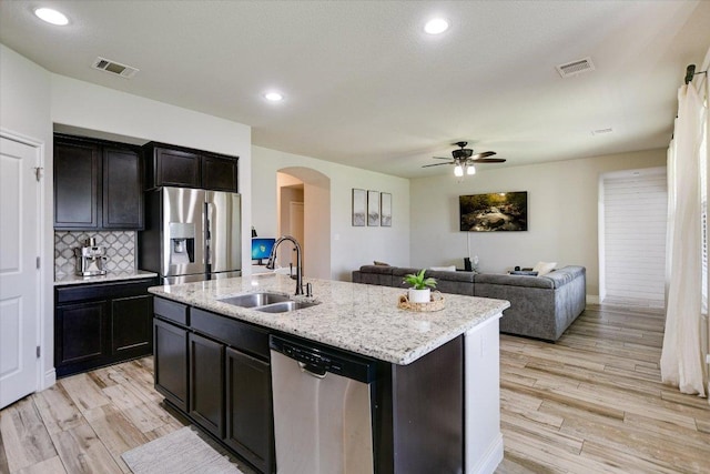 kitchen featuring stainless steel appliances, a sink, arched walkways, ceiling fan, and light wood-type flooring
