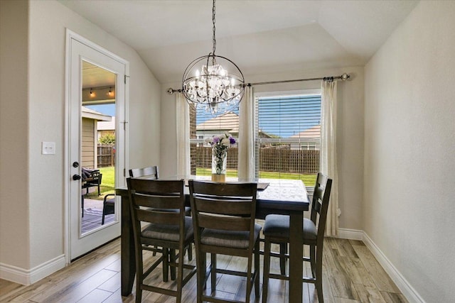 dining space with a chandelier, light wood finished floors, baseboards, and lofted ceiling