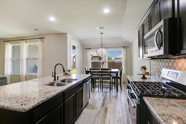 5659 Corsica Loop, Round Rock, TX 78665 - kitchen featuring stainless steel appliances, a sink, dark cabinetry, light wood-style flooring, and a center island with sink