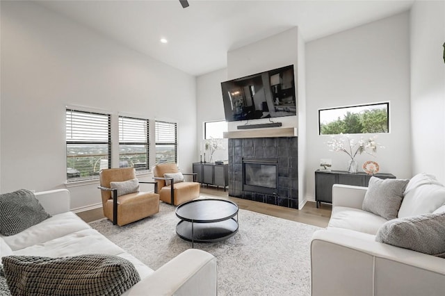 living room featuring high vaulted ceiling, a tile fireplace, wood finished floors, baseboards, and recessed lighting