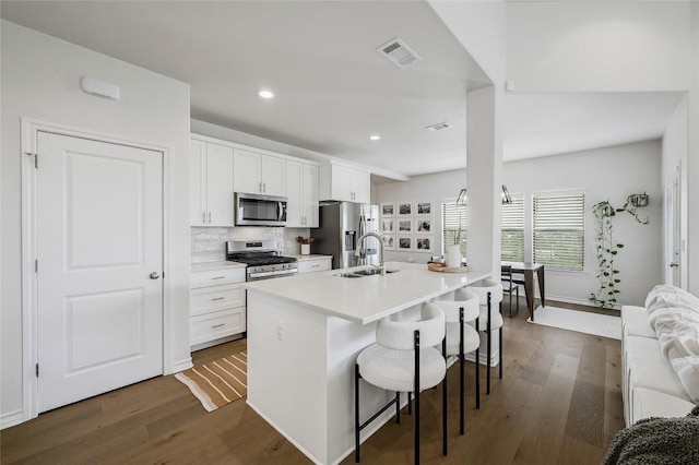 kitchen with stainless steel appliances, a breakfast bar area, a sink, white cabinetry, and dark wood-type flooring