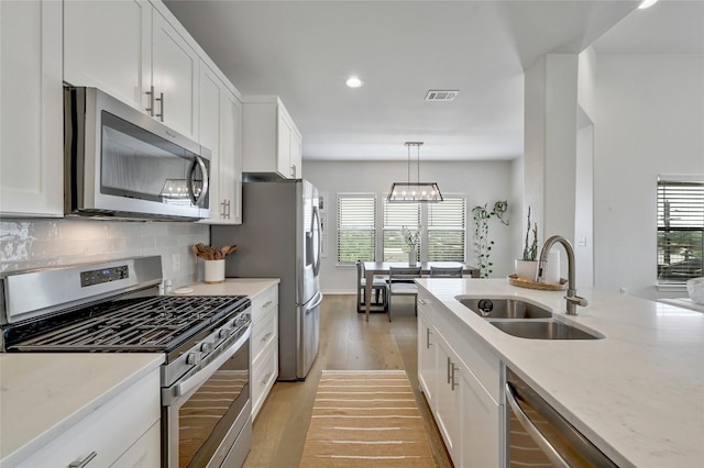 kitchen with stainless steel appliances, a sink, light wood finished floors, white cabinetry, and recessed lighting