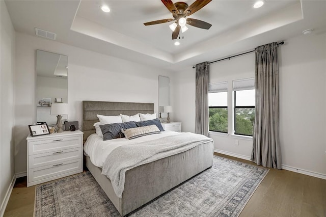 bedroom with a raised ceiling, recessed lighting, baseboards, light wood-style floors, and ceiling fan