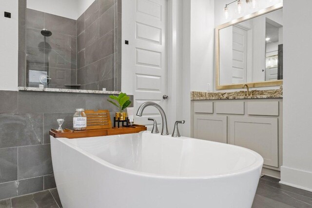 124 Low River Ln, Georgetown, TX 78628 - bathroom featuring a freestanding tub, vanity, a walk in shower, tile patterned flooring, and tile walls