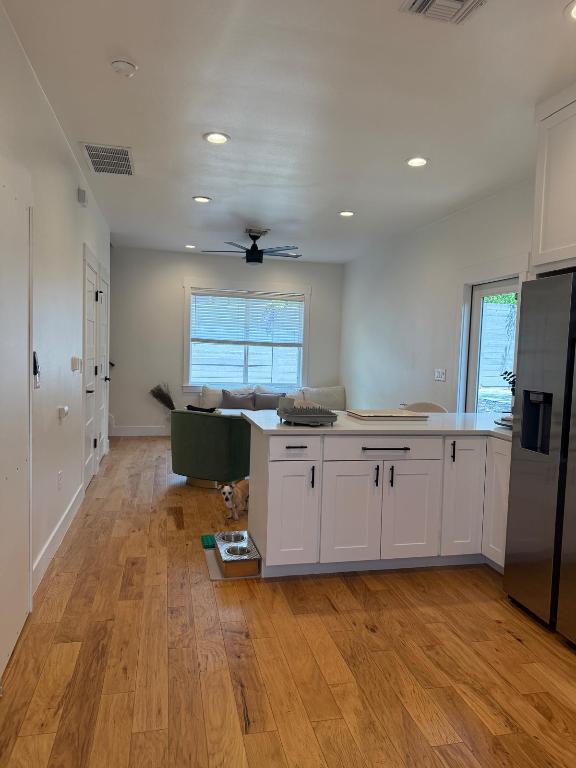 kitchen with stainless steel fridge with ice dispenser, a peninsula, light wood-style flooring, white cabinetry, and open floor plan
