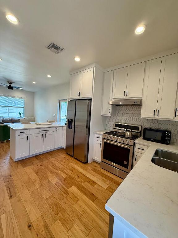 kitchen with stainless steel appliances, under cabinet range hood, a sink, a peninsula, and light wood finished floors