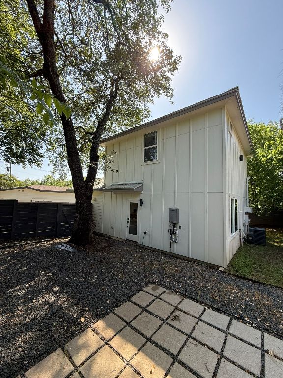 rear view of house with board and batten siding, a patio, cooling unit, and fence