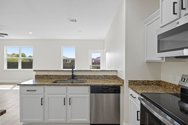 kitchen featuring appliances with stainless steel finishes, a sink, dark stone counters, white cabinetry, and recessed lighting