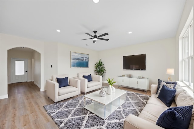 living room with arched walkways, a ceiling fan, light wood-style floors, recessed lighting, and baseboards