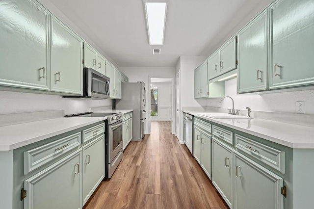 kitchen with stainless steel appliances, a sink, green cabinetry, and wood finished floors