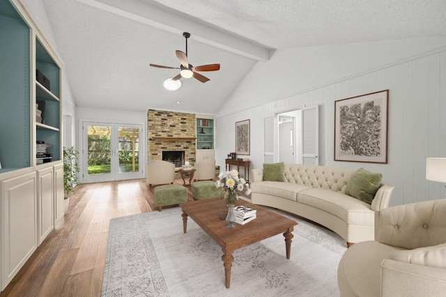 living area featuring wood finished floors, a ceiling fan, built in features, a brick fireplace, and a textured ceiling