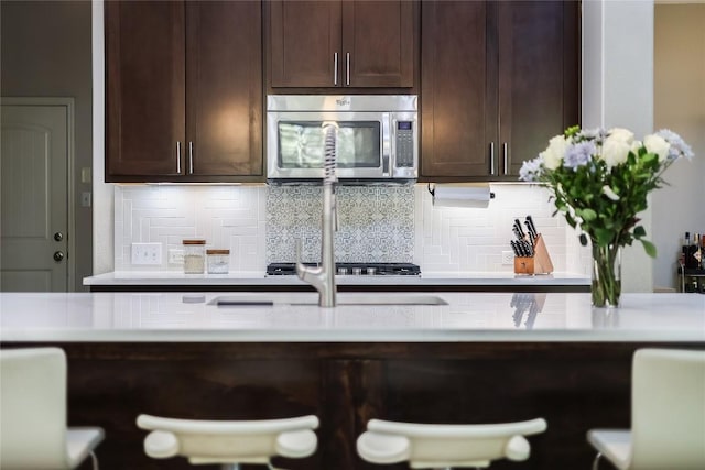 402 Dry Gulch Bnd, Cedar Park, TX 78613 - kitchen featuring stainless steel microwave, dark brown cabinetry, backsplash, and light countertops