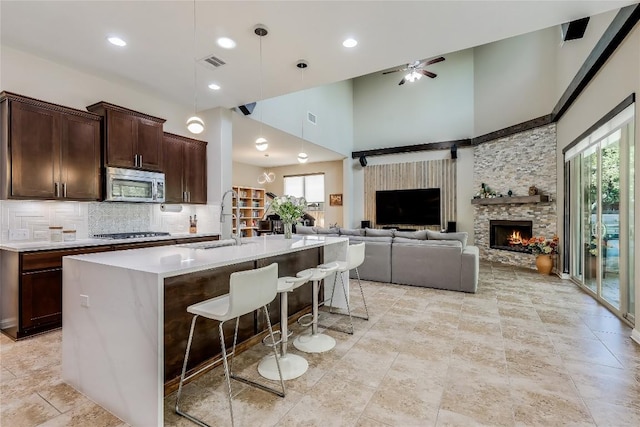 402 Dry Gulch Bnd, Cedar Park, TX 78613 - kitchen with stainless steel microwave, a stone fireplace, a ceiling fan, a towering ceiling, and gas stovetop