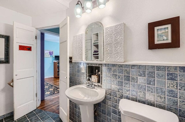 bathroom featuring toilet, tile walls, a sink, wainscoting, and wood finished floors
