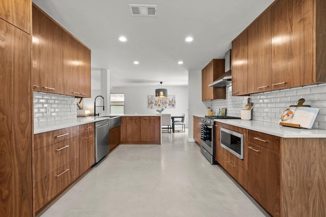 11701 Tanglebriar Trl, Austin, TX 78750 - kitchen with a peninsula, wall chimney exhaust hood, stainless steel appliances, brown cabinetry, and recessed lighting