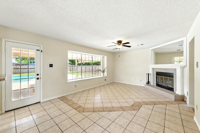 unfurnished living room featuring light tile patterned flooring, plenty of natural light, ceiling fan, and a textured ceiling