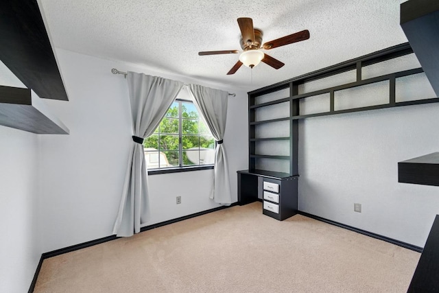 unfurnished office featuring light colored carpet, a ceiling fan, a textured ceiling, and baseboards