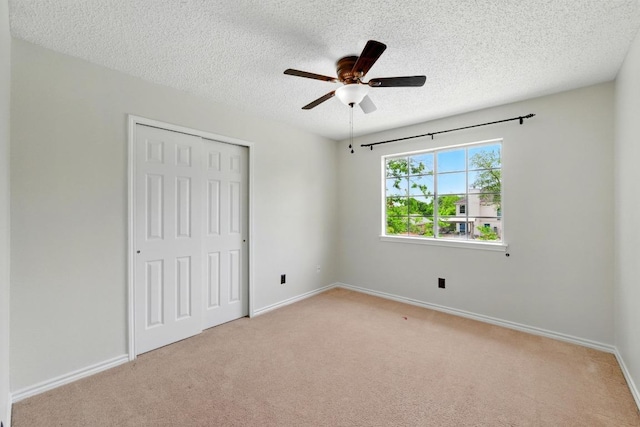 unfurnished bedroom with a closet, a textured ceiling, carpet floors, baseboards, and ceiling fan