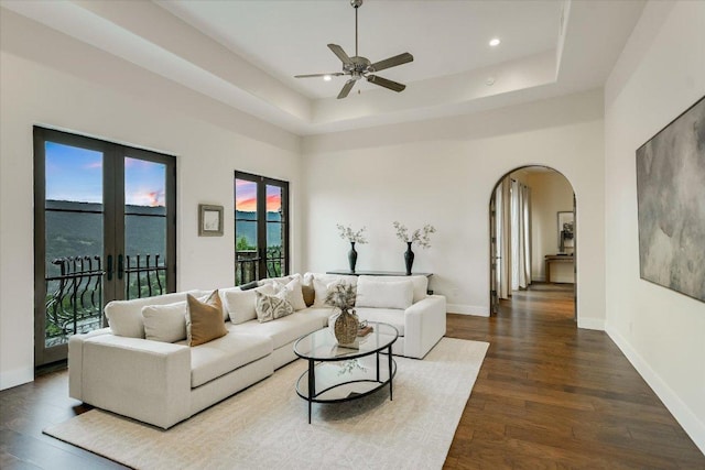 12861 Hughes Park Rd, Austin, TX 78732 - living room featuring arched walkways, wood finished floors, a ceiling fan, a tray ceiling, and baseboards