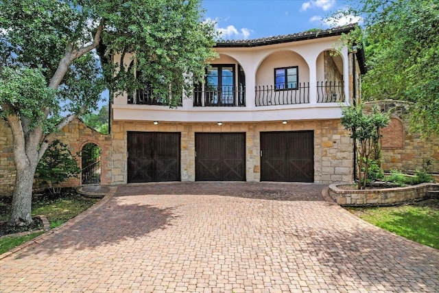 12861 Hughes Park Rd, Austin, TX 78732 - mediterranean / spanish house featuring a balcony, stucco siding, decorative driveway, an attached garage, and stone siding