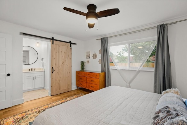 8907 Hunters Trce, Austin, TX 78758 - bedroom featuring a barn door, light wood-type flooring, a sink, ensuite bathroom, and baseboards