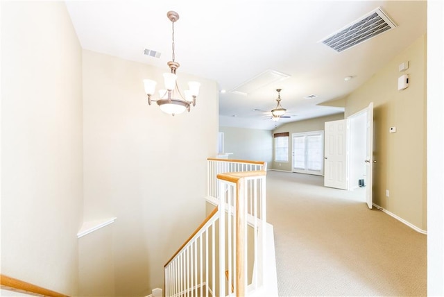 hall featuring an upstairs landing, a chandelier, light carpet, baseboards, and attic access