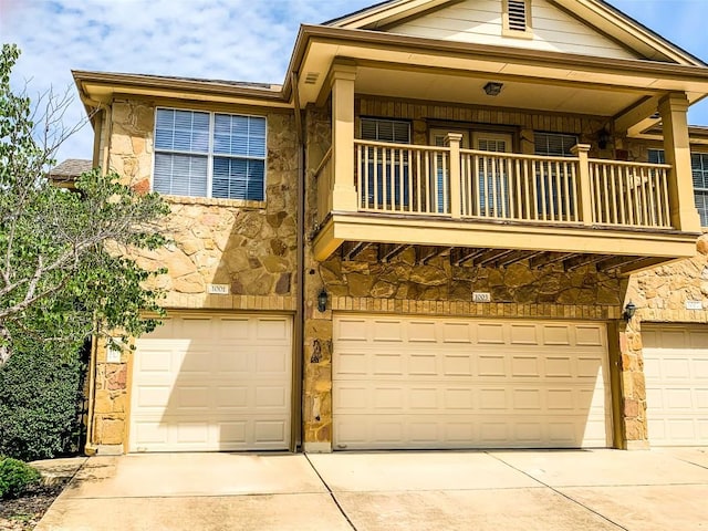 view of property featuring a balcony, an attached garage, stone siding, and driveway